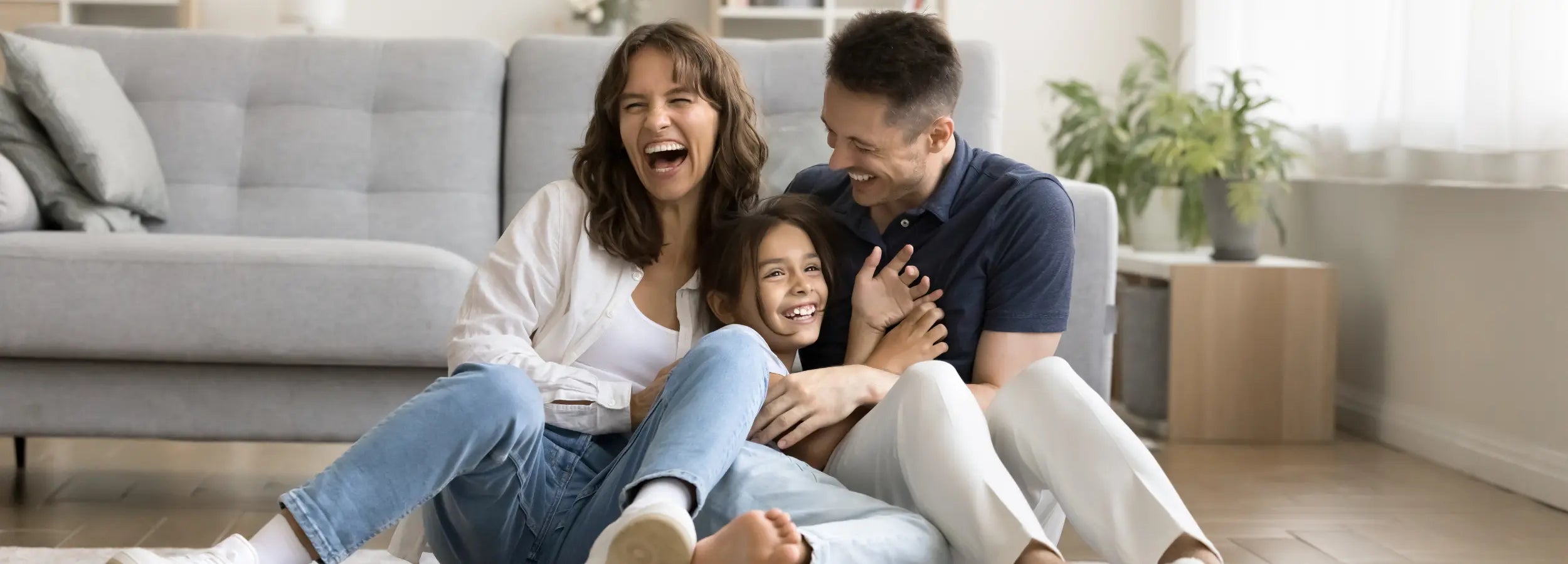 parents with a child laughing sitting on the floor of a living room